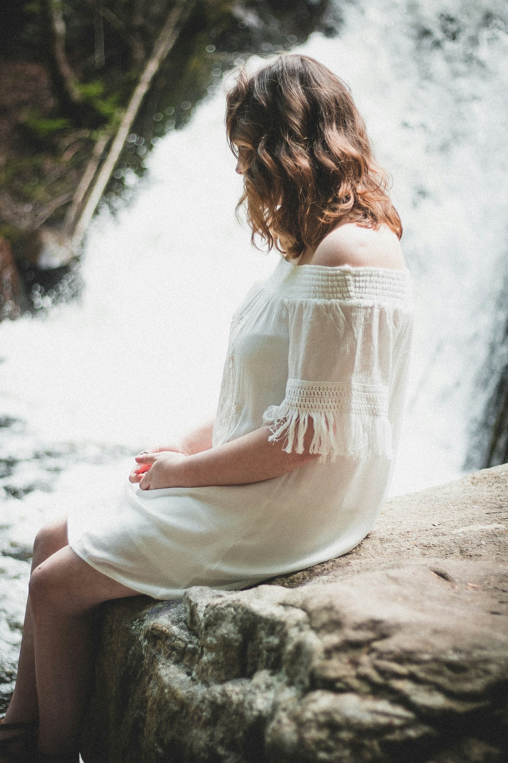 woman sitting on rock beside waterfall at daytime